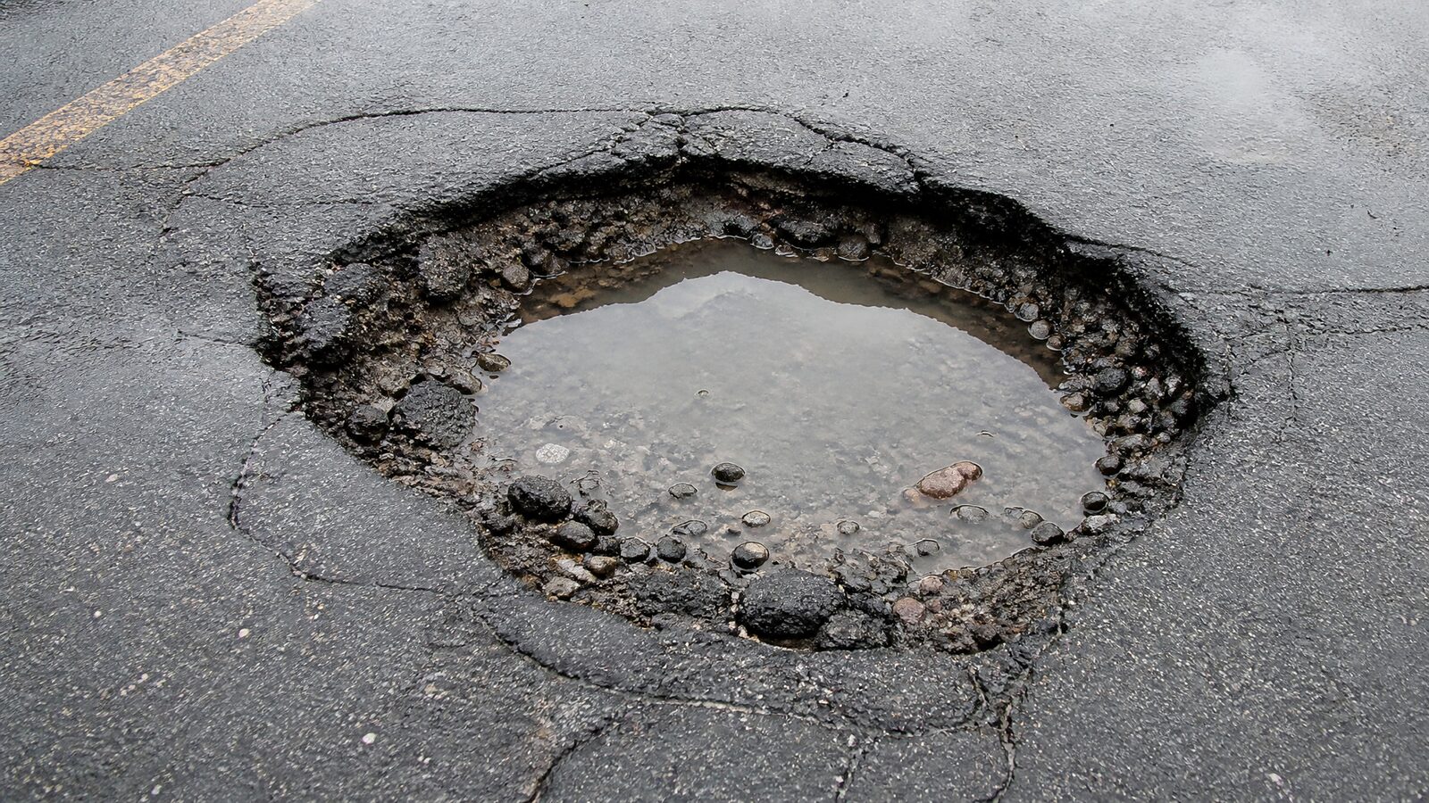 Pothole in an asphalt parking lot with water pooling and crumbled edges in Virginia